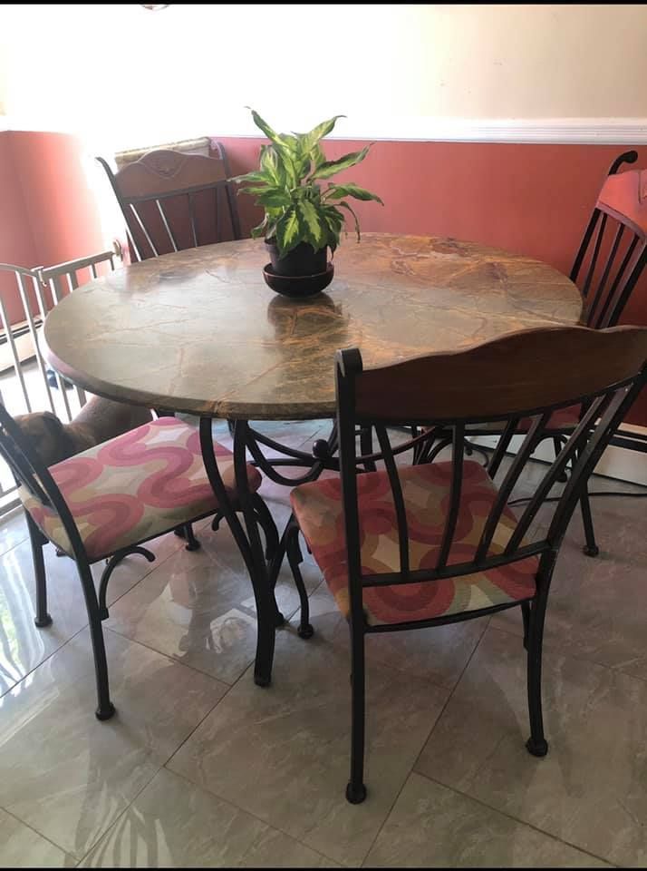Round dining table with four wrought-iron chairs and a potted plant in a tiled room