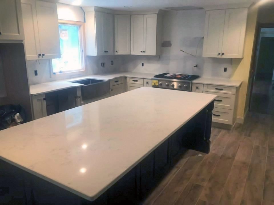 Bright modern kitchen with large white island, white cabinets, and wood-look flooring.