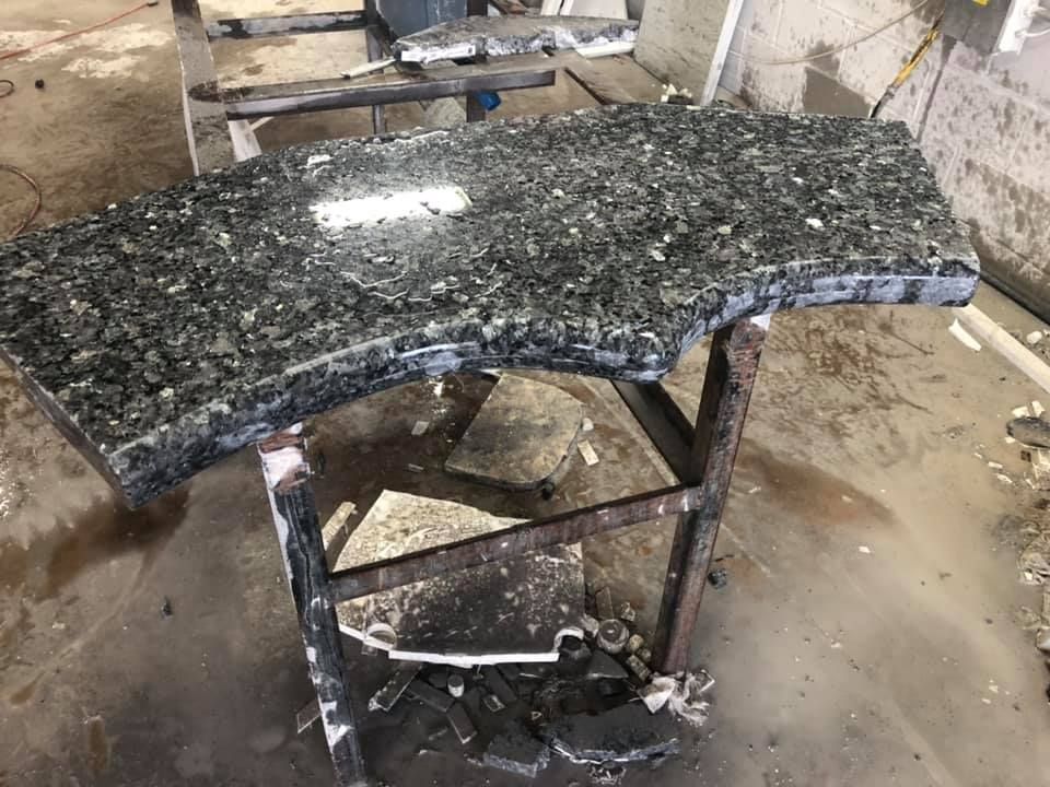 Broken black granite tabletop on a metal frame in a dusty workshop.