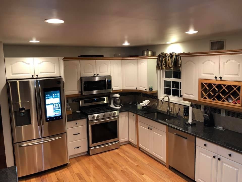 Modern kitchen with stainless steel appliances, white cabinets, black countertops, and hardwood floors