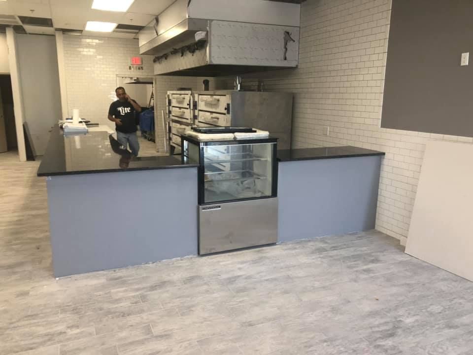 Empty commercial kitchen with blue counter and stainless steel oven; person walking in the background