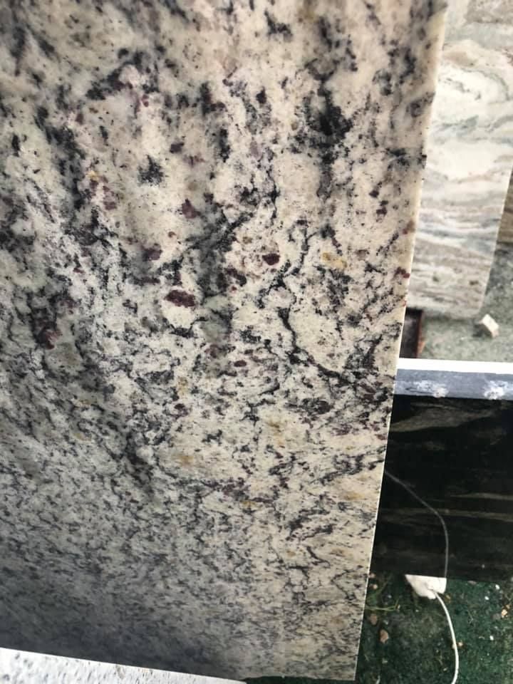 Close-up of a speckled gray, black, and beige granite slab in a stone yard