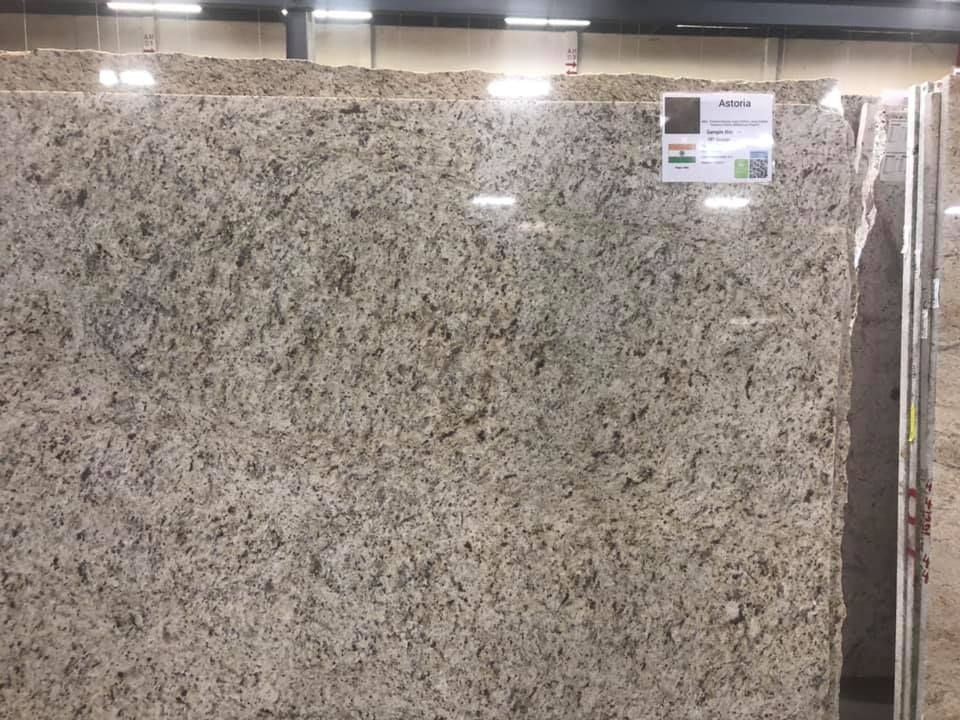 Large polished granite slab with speckled gray, beige, and black pattern in a showroom.