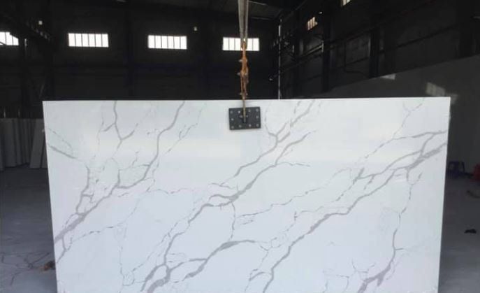 Large white marble-look slab with gray veining hanging in an industrial warehouse.
