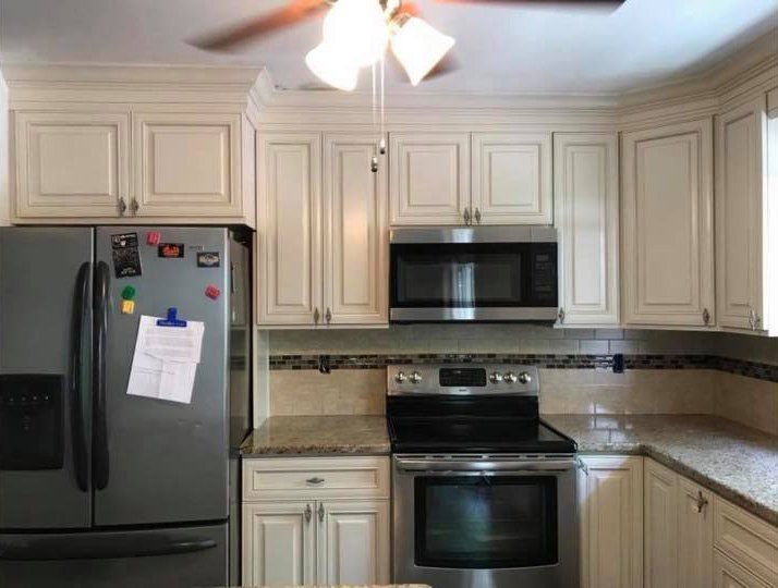 Small beige kitchen with stainless steel fridge, stove, microwave, and ceiling fan