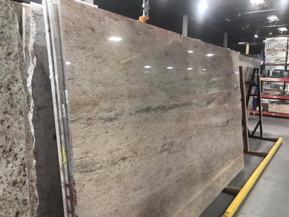 Large beige granite slab displayed upright in a warehouse or stone showroom