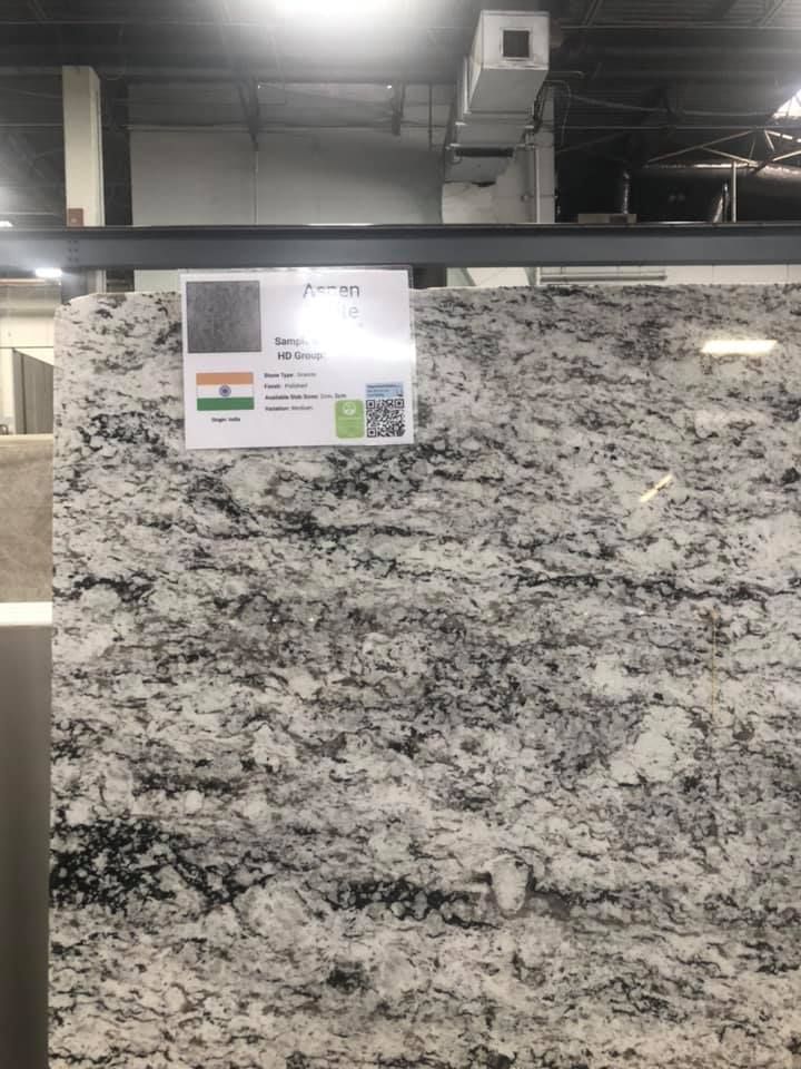 Large gray-and-white granite slab displayed in a warehouse, with a sample label attached.