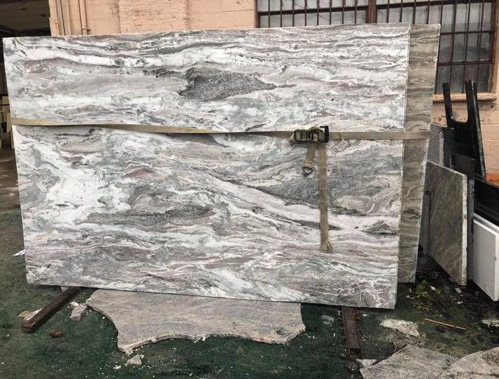 Large white and gray marble slab held upright outdoors with a clamp and stand