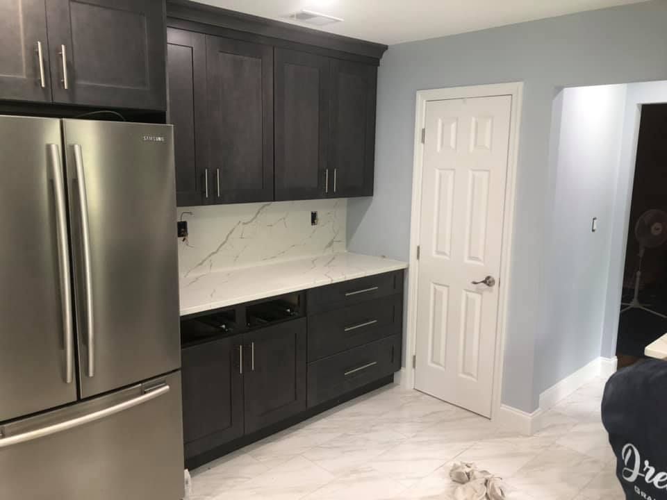 Modern kitchen with dark cabinets, stainless steel refrigerator, white countertops, and light tile floor