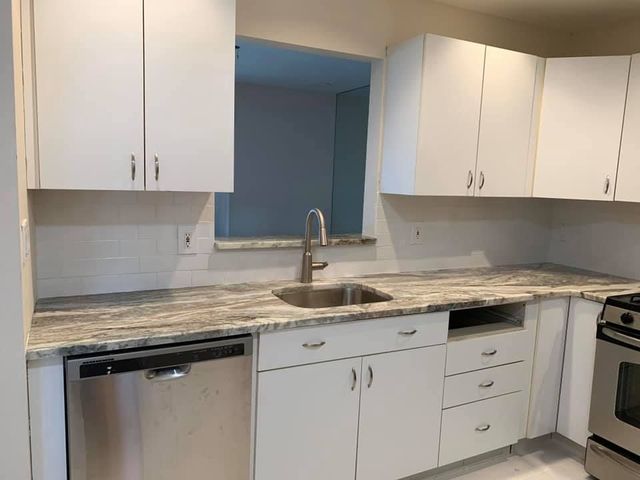 Modern white kitchen with granite countertops, sink, dishwasher, and stove under white cabinets.