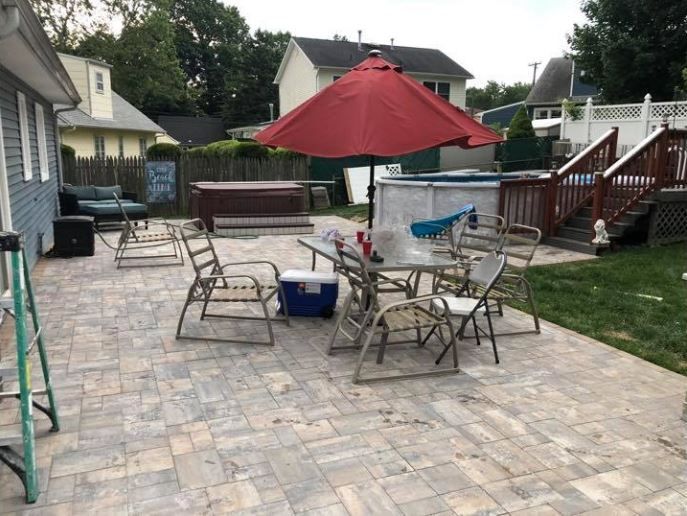 Patio with red umbrella, metal table and chairs, grill, and cooler in a suburban backyard