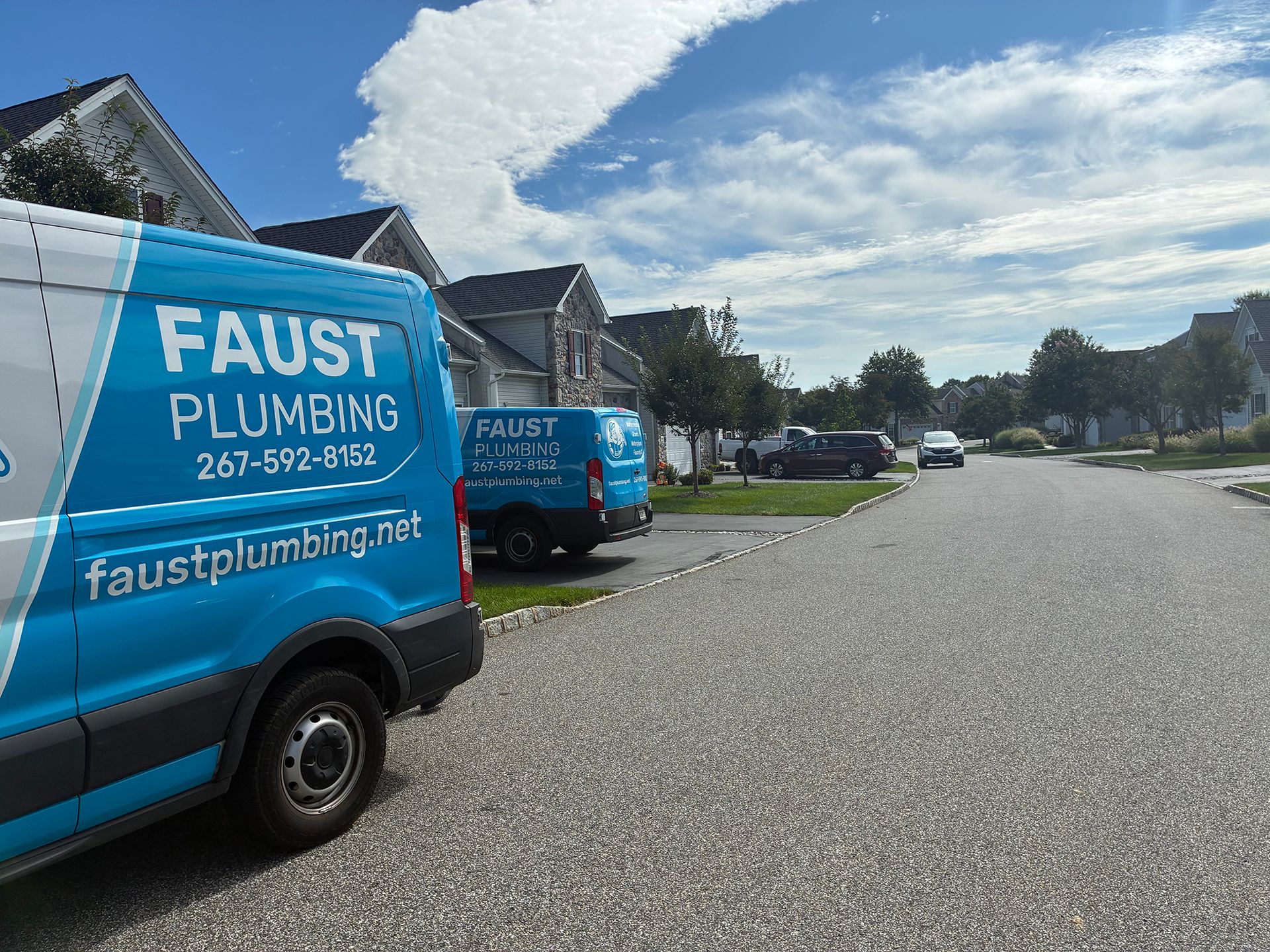 Blue Faust Plumbing vans parked along a quiet residential street under a bright sky.