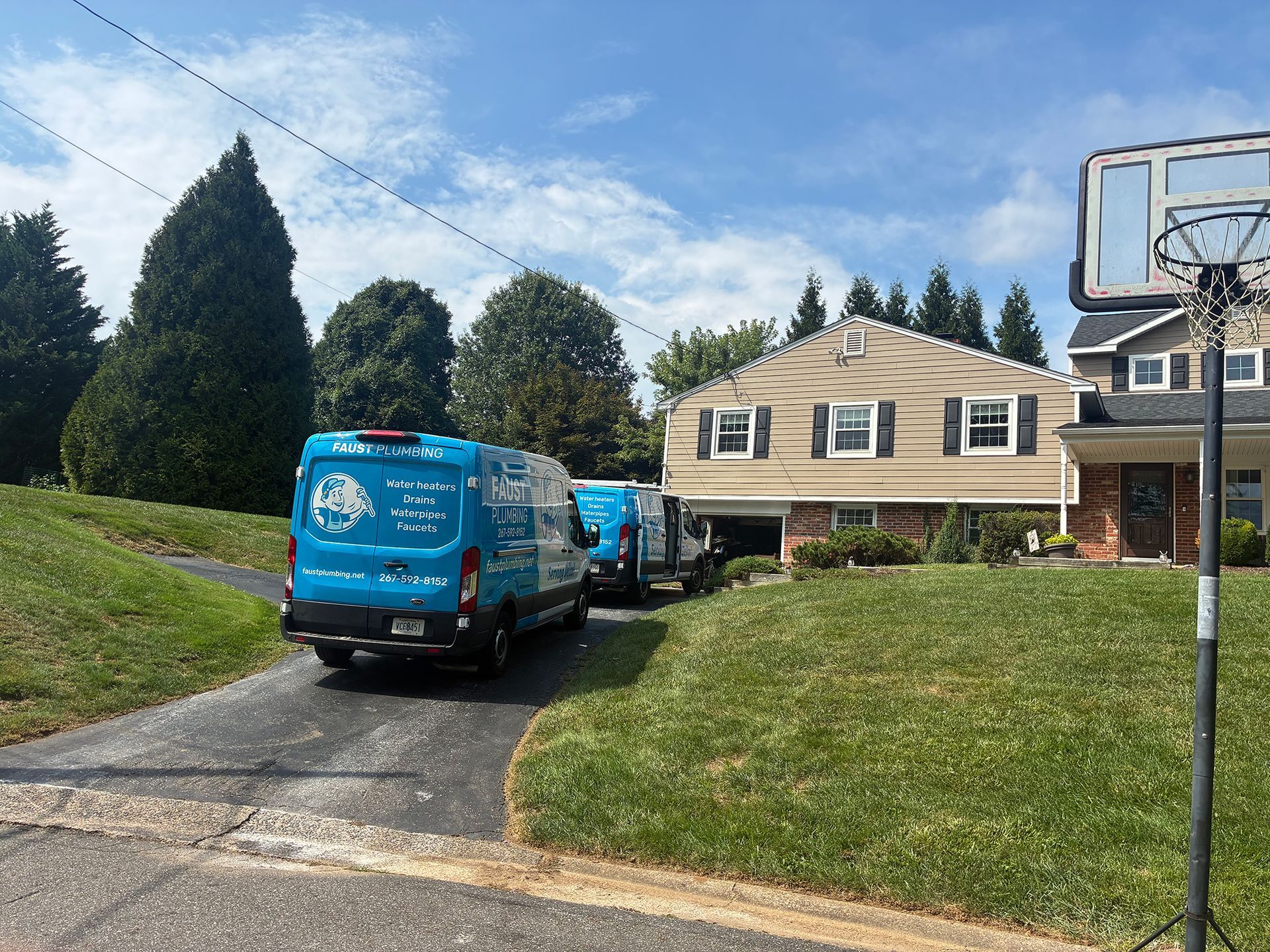 Blue utility vans parked in a driveway beside a beige house on a grassy suburban hill.