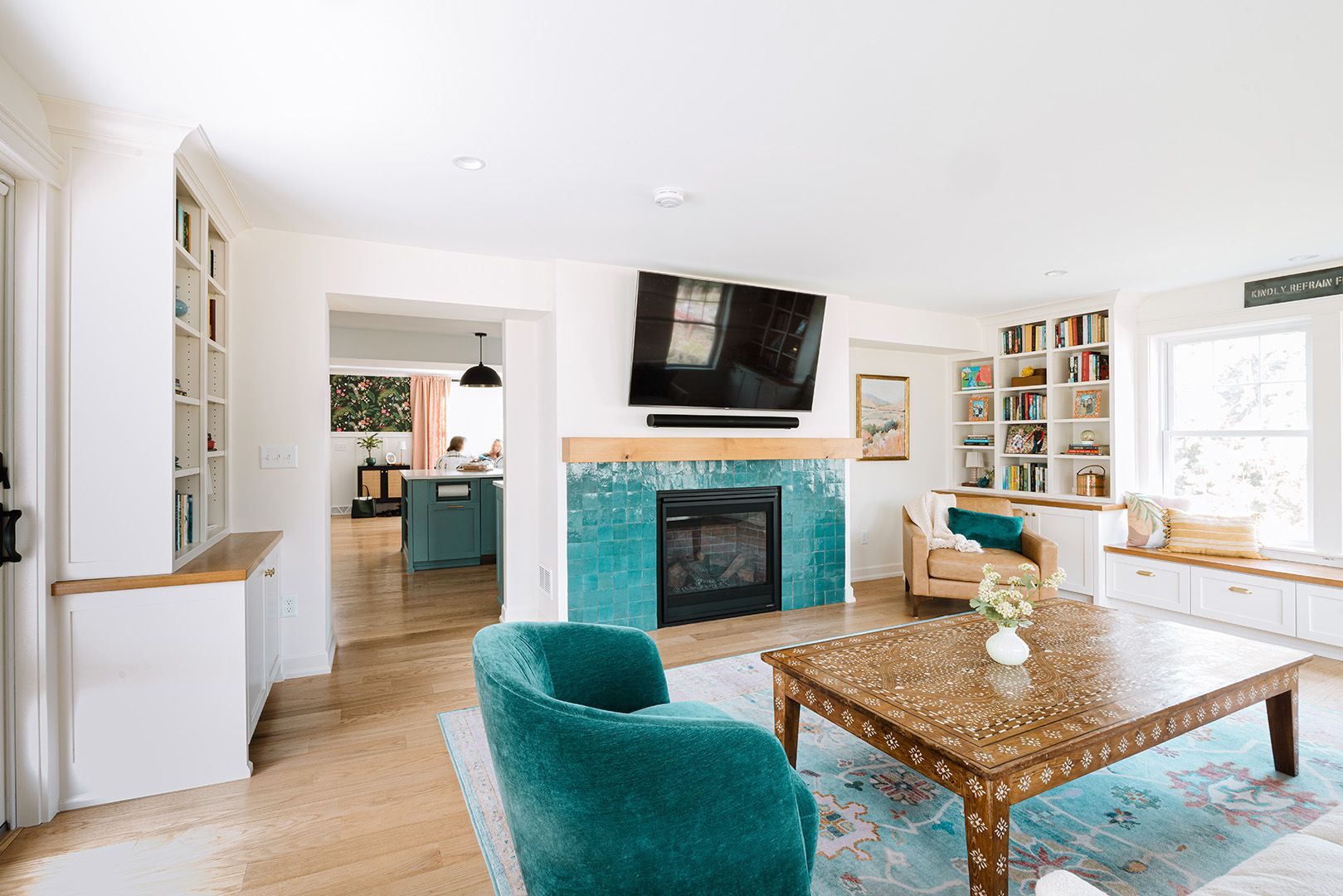 Bright living room with teal chairs, stone fireplace, large TV, and a wood coffee table