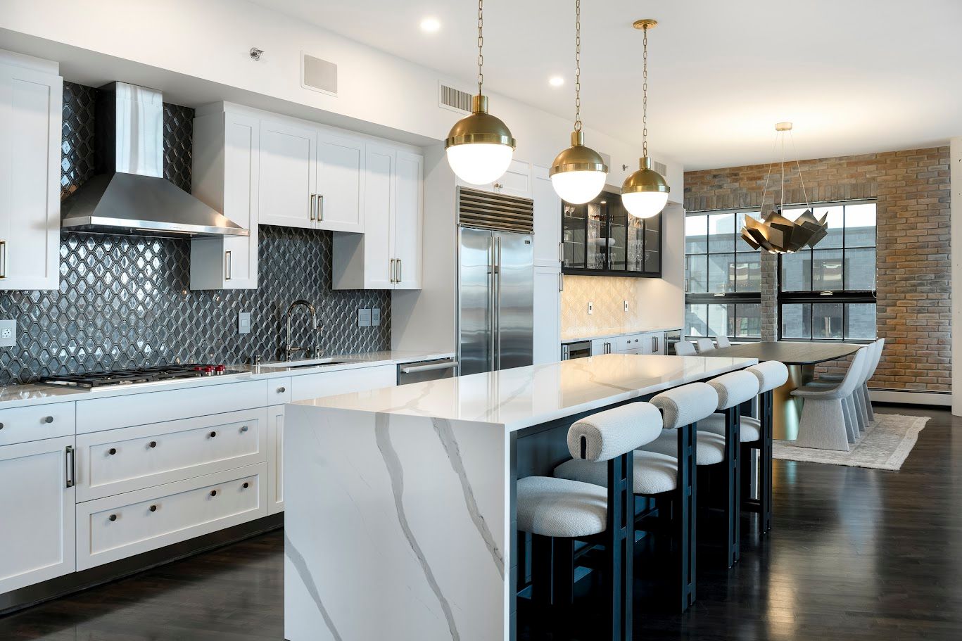 Modern white kitchen with island, pendant lights, stainless steel appliances, and dark flooring.