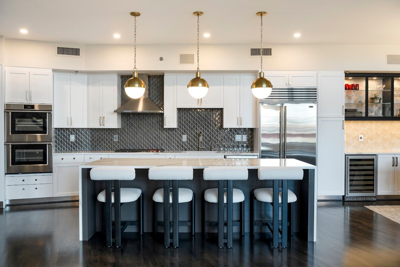 Modern kitchen with white cabinets, island with stools, and pendant lights.