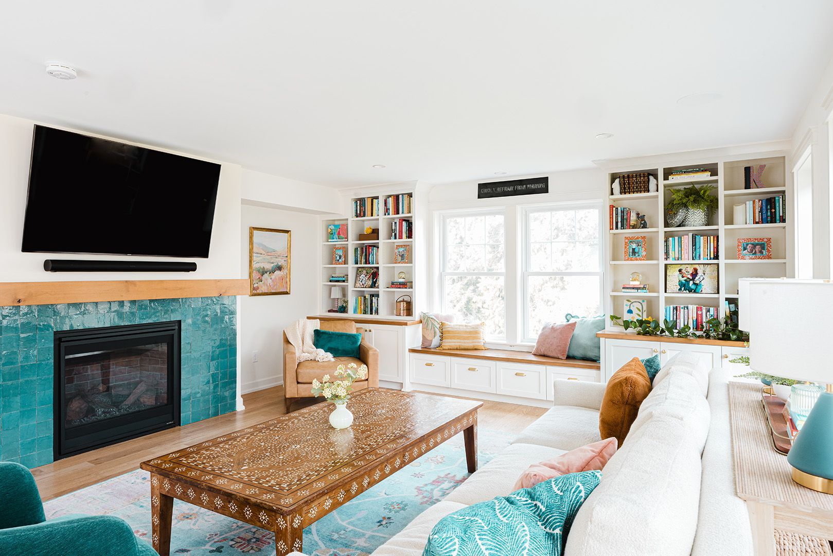 Bright living room with teal fireplace, white built-ins, and a large wall-mounted TV