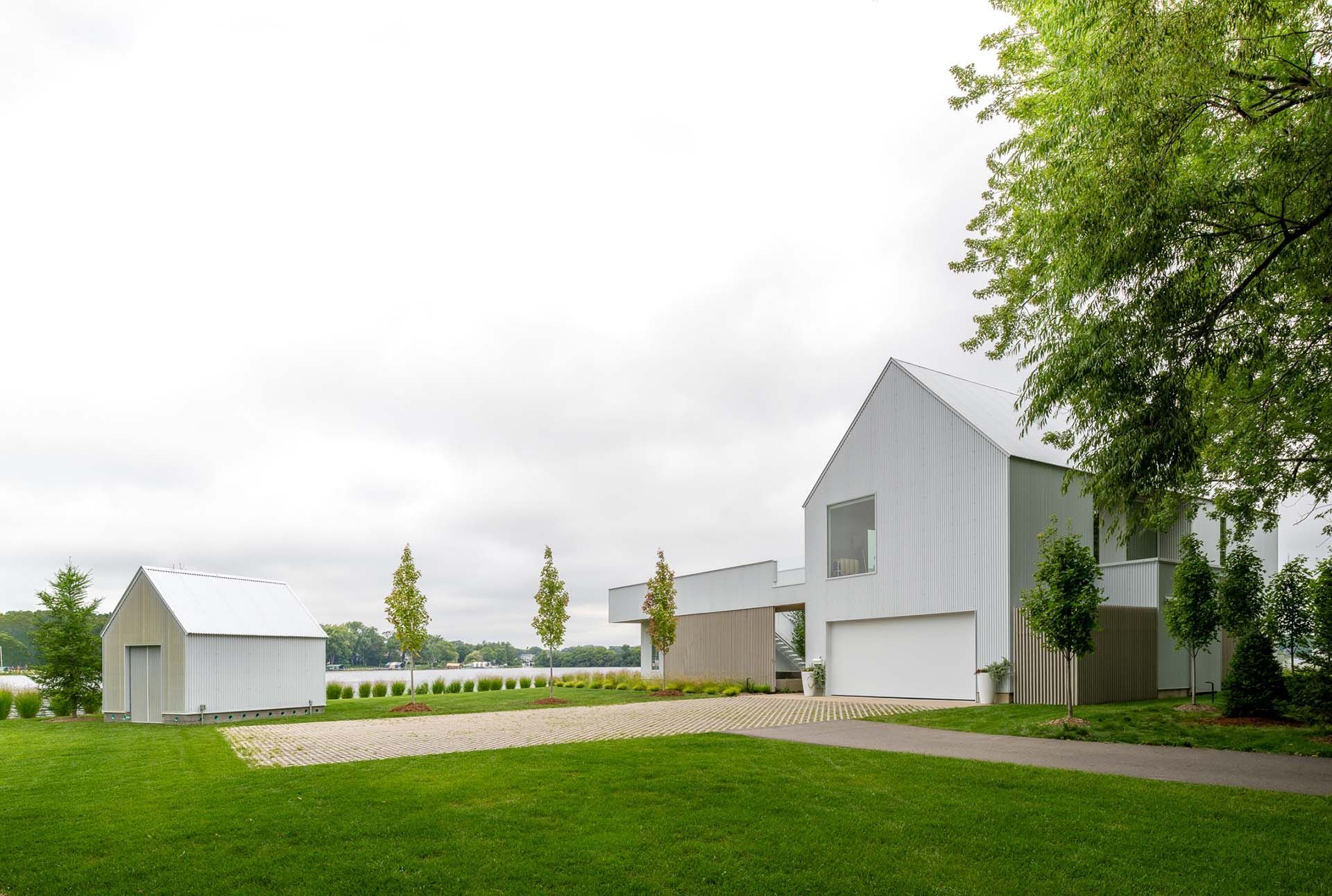 A modern white house with a shed or small barn and lush green property.