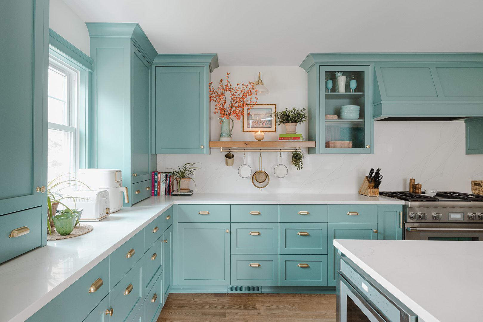 Mint-green kitchen with white countertops, open shelves, and a gas range under a window