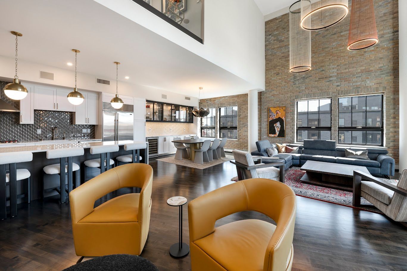Modern open-plan living space with kitchen, dining, and seating areas. Brick accent wall and yellow chairs.