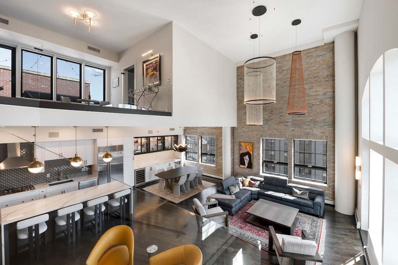 Spacious, modern loft interior with high ceilings, exposed brick, and a mezzanine level.