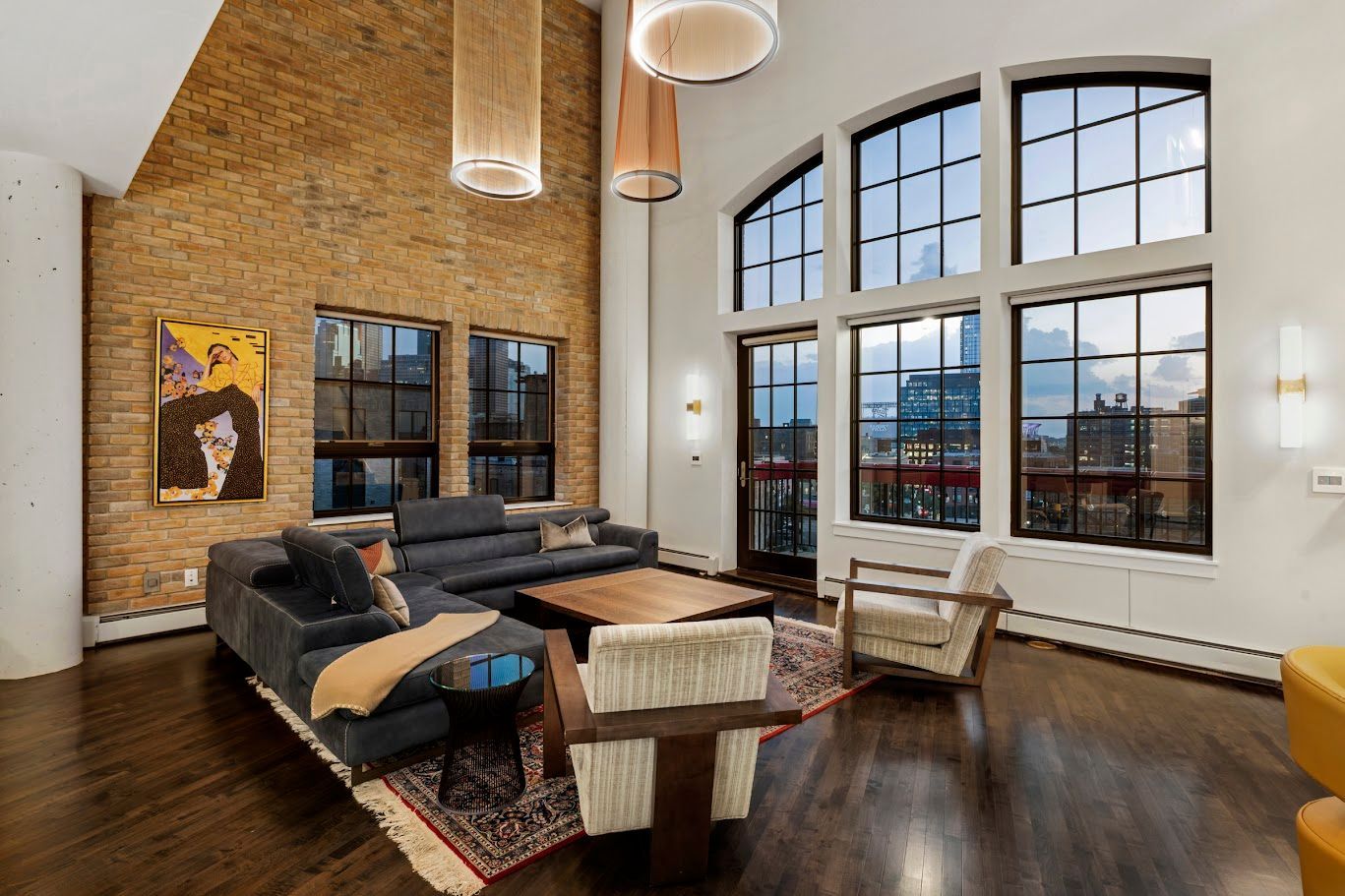 Living room with exposed brick wall, large windows, and modern furniture.