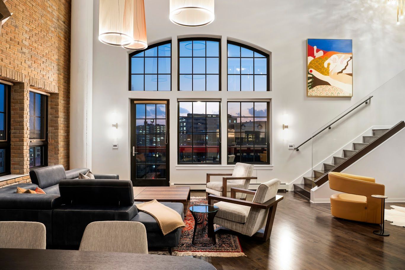 Living room with large arched windows, exposed brick wall, dark wood floors, and modern furniture.