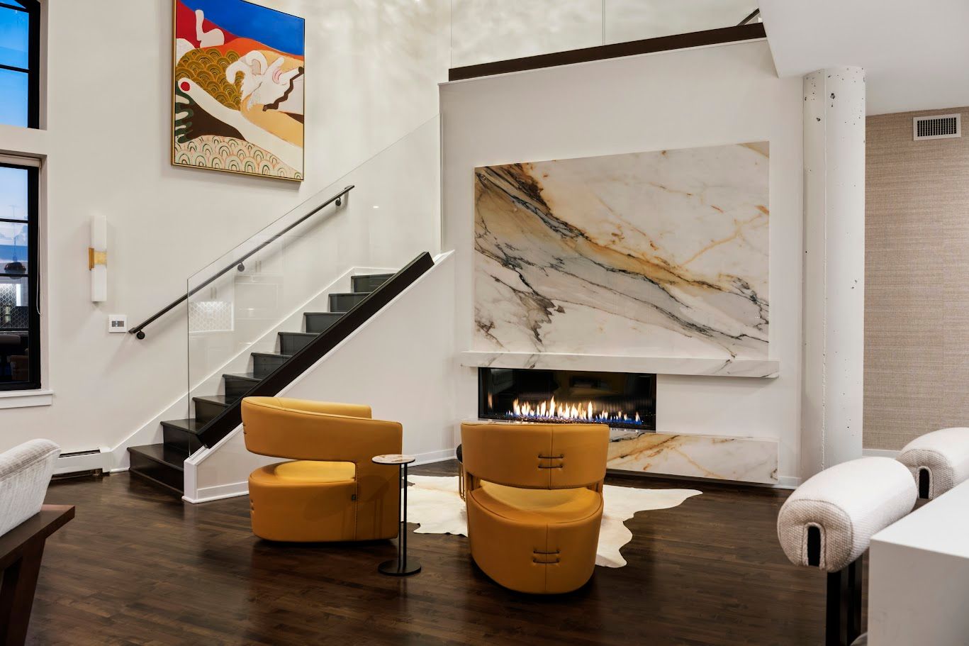 Living room with fireplace, stairs, and two yellow chairs. Marble fireplace backdrop. Dark hardwood floors.