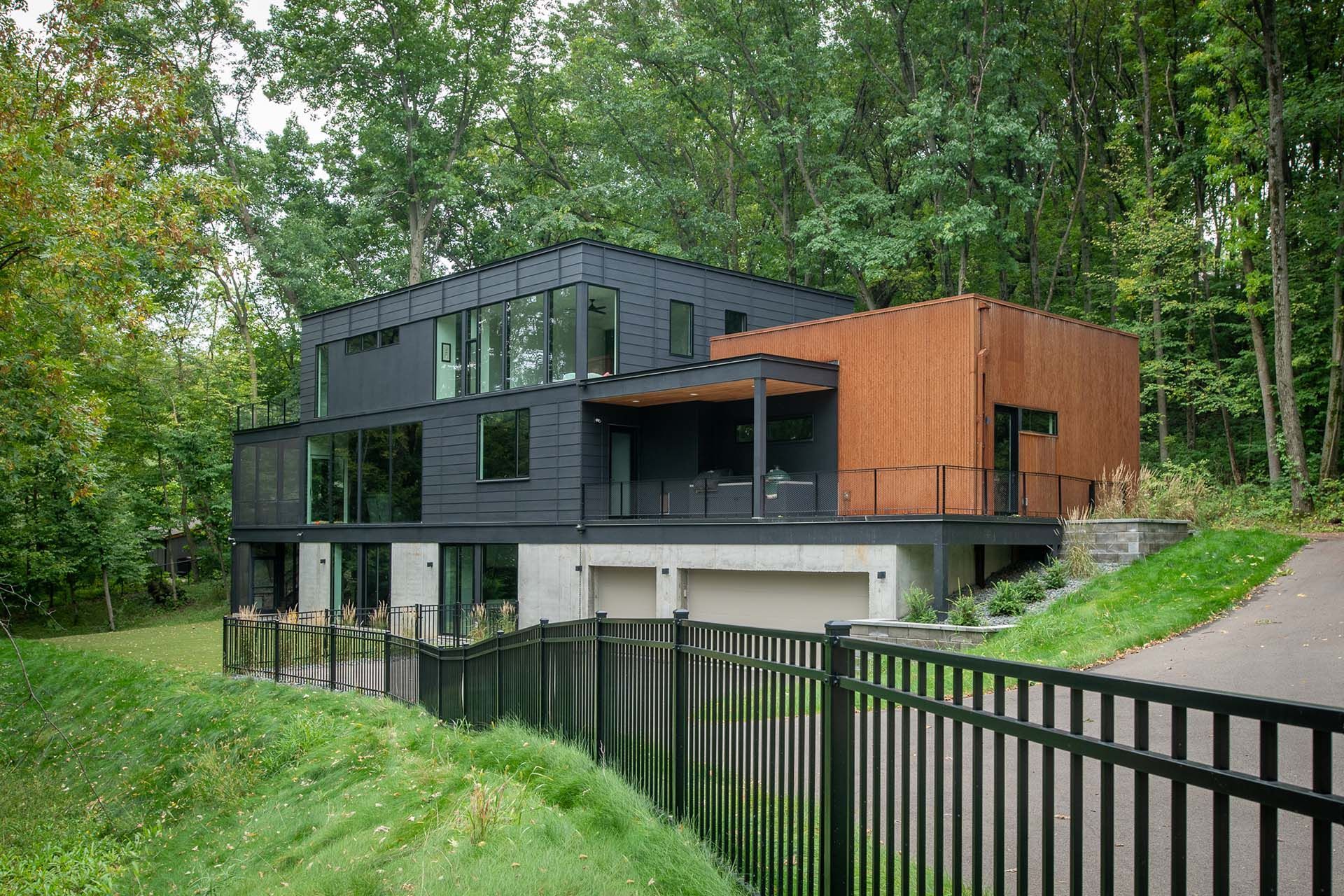A large black house is surrounded by trees and a black fence.