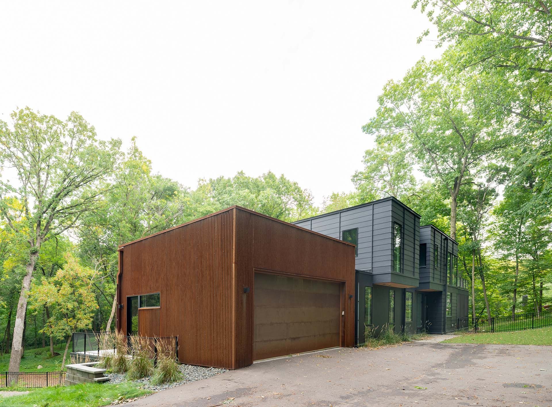 A modern house with a garage is surrounded by trees.