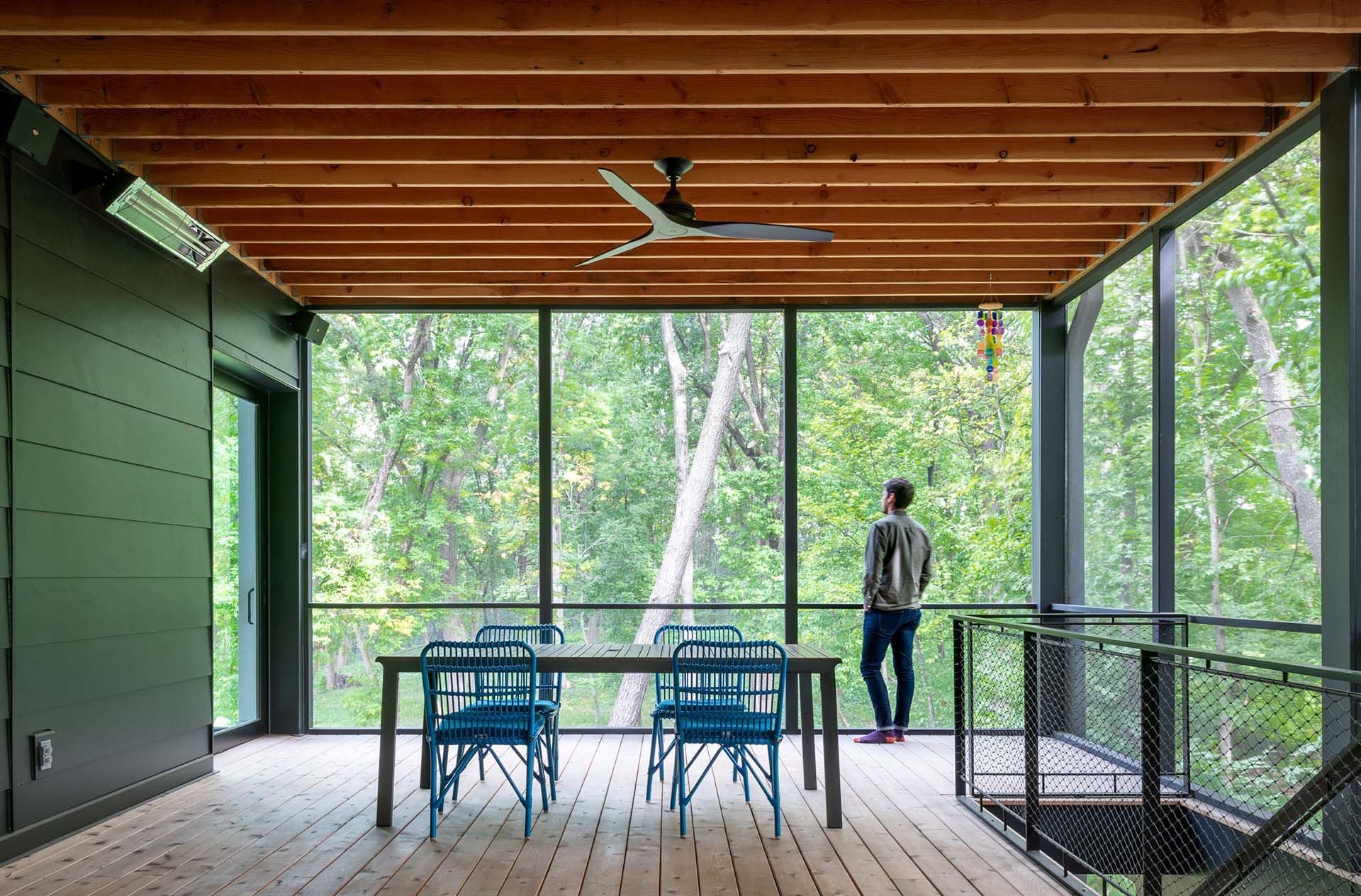 A man is standing on a screened in porch looking out at the trees.
