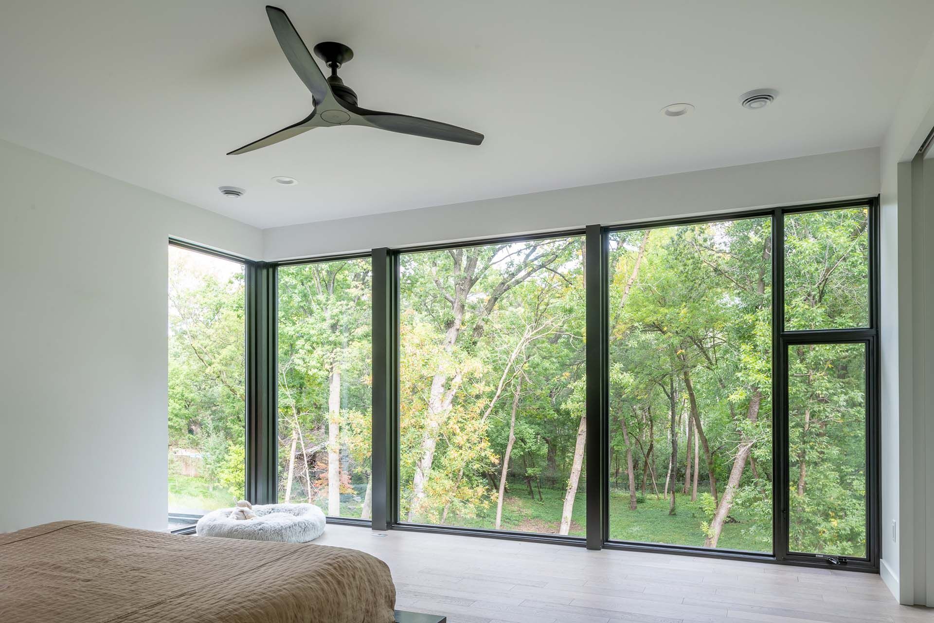A bedroom with a large window and a ceiling fan.