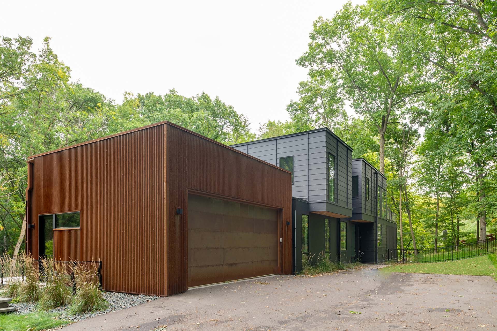 A modern house with a garage and a driveway surrounded by trees.