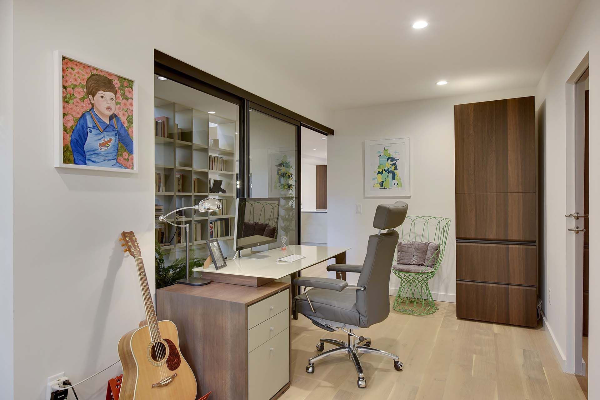 A room with a desk , chair , guitar and painting on the wall.