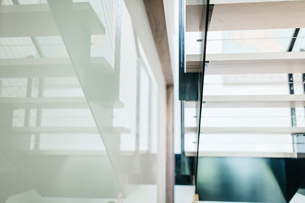 A staircase with a glass railing and a white wall.