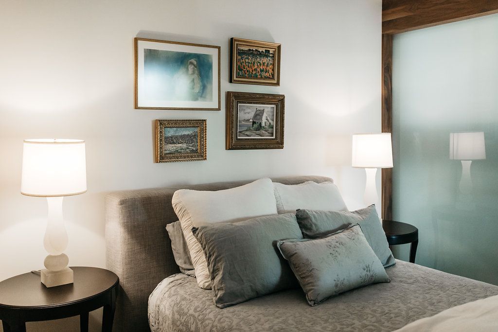 A bedroom with a bed , lamps , nightstands and paintings on the wall.