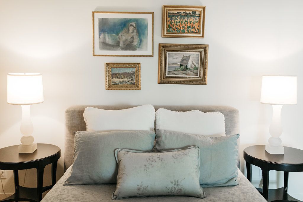 A bedroom with a bed , lamps , and paintings on the wall.