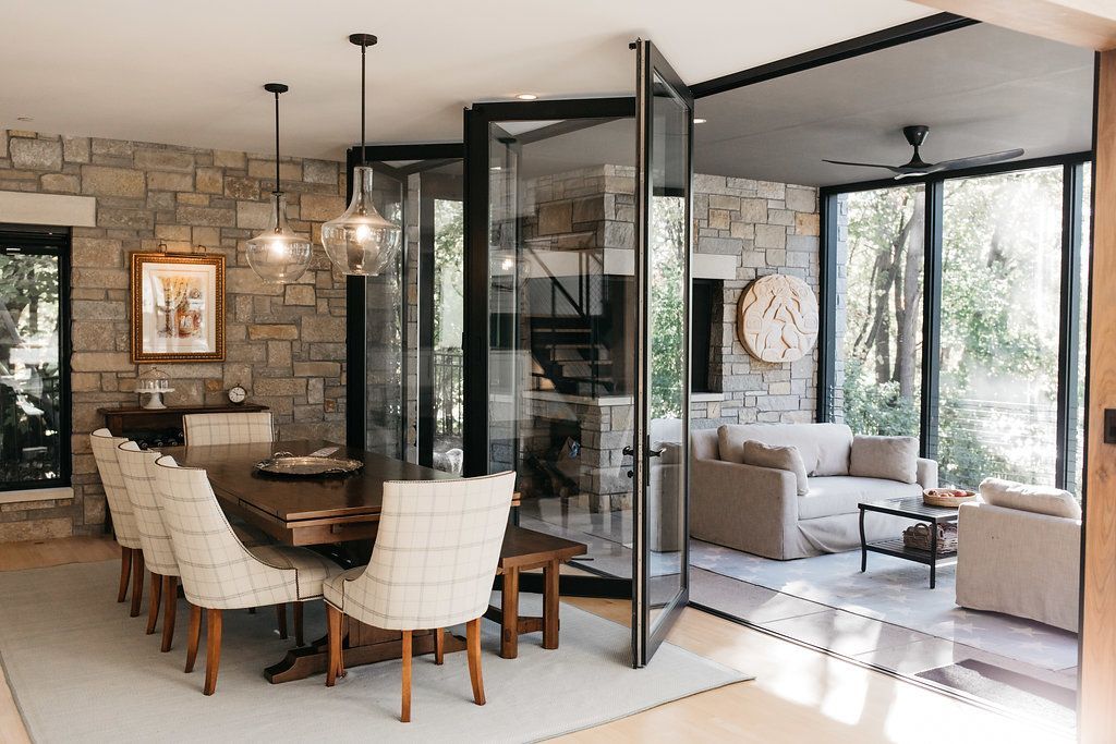A dining room with a table and chairs and a living room with a lot of windows.