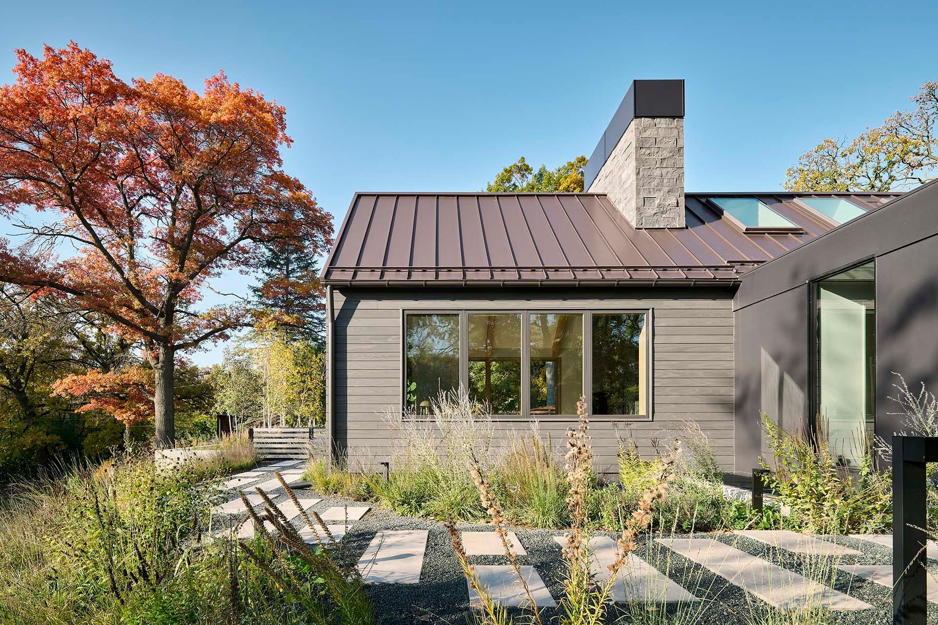 A house with a chimney on the roof is surrounded by trees and bushes.