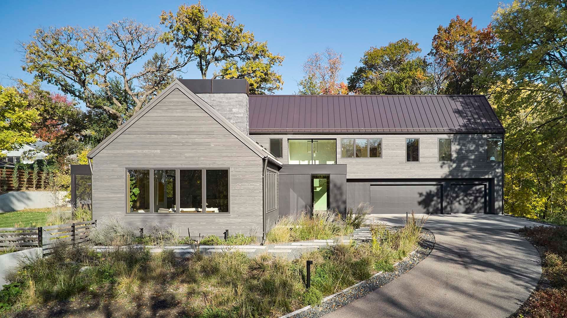 A large house with a black roof is surrounded by trees and bushes.
