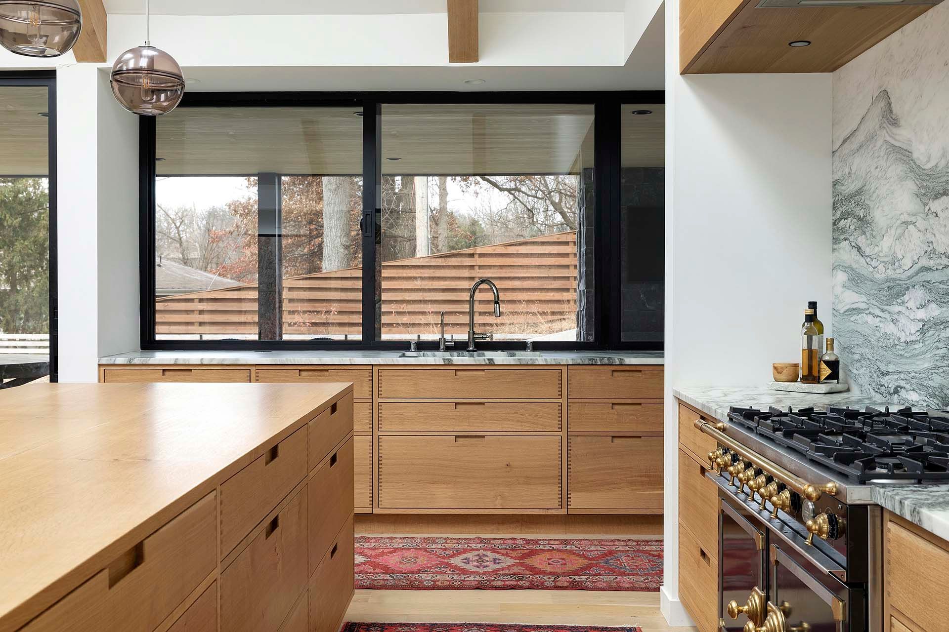 A kitchen with wooden cabinets , a stove , a sink and a large window.