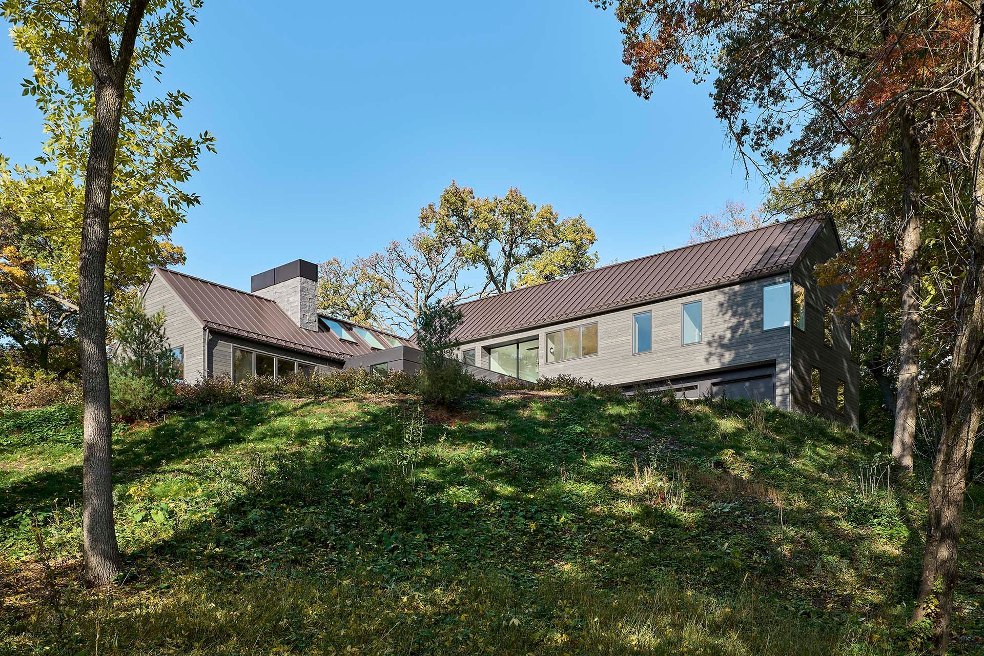 A large house is sitting on top of a grassy hill surrounded by trees.