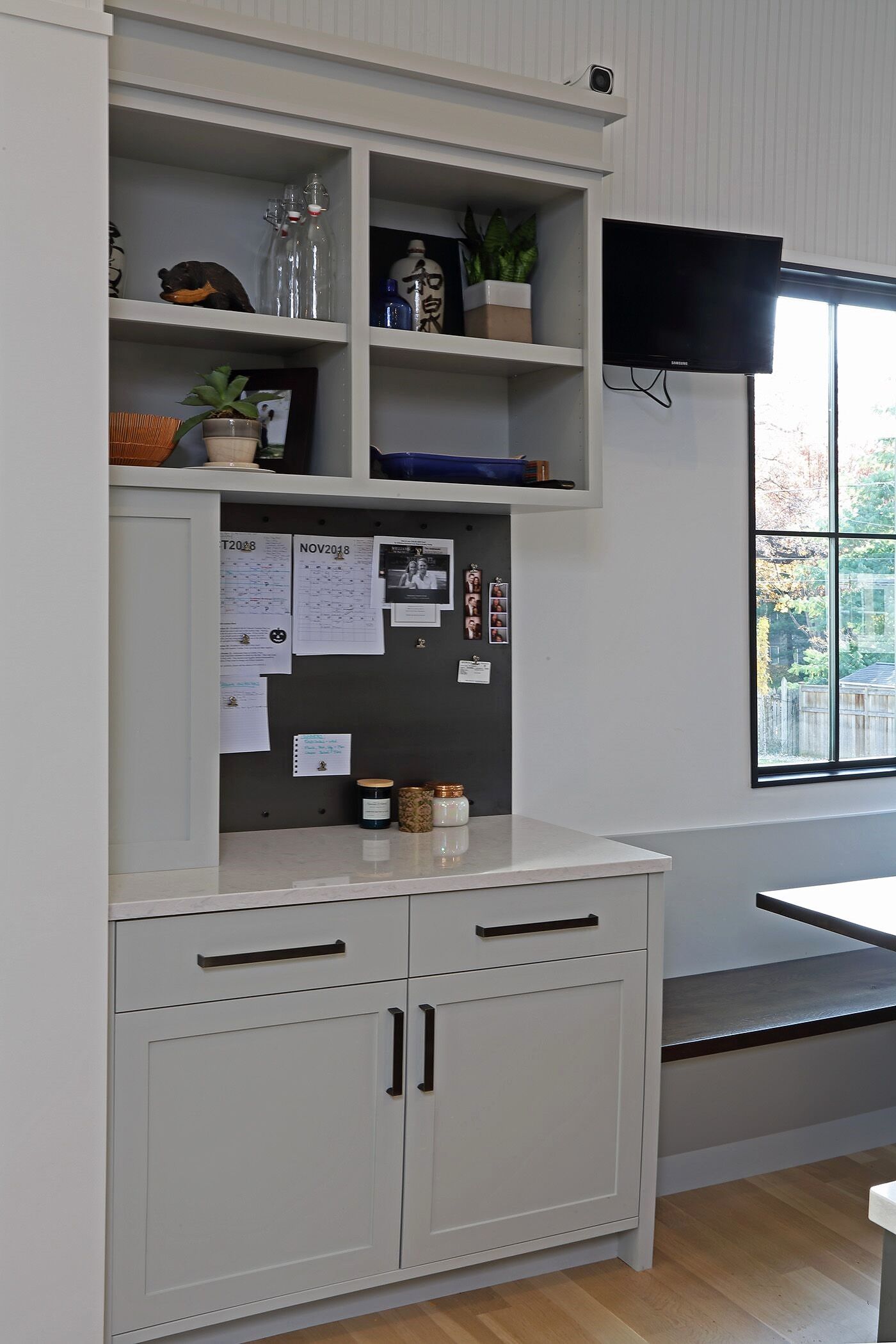 A kitchen with a table , cabinets , shelves and a bulletin board.