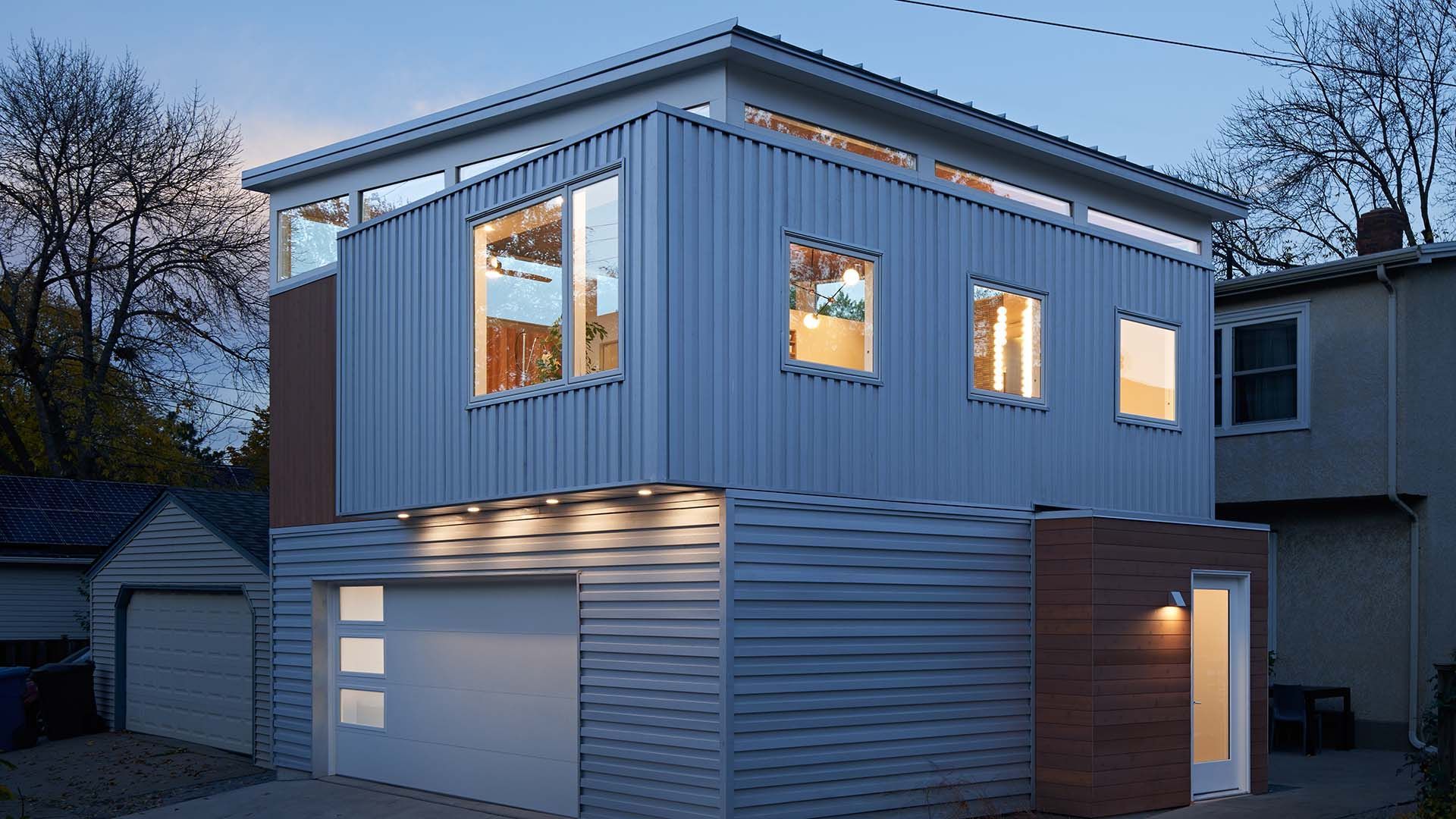 A house with a garage and a lot of windows is lit up at night.