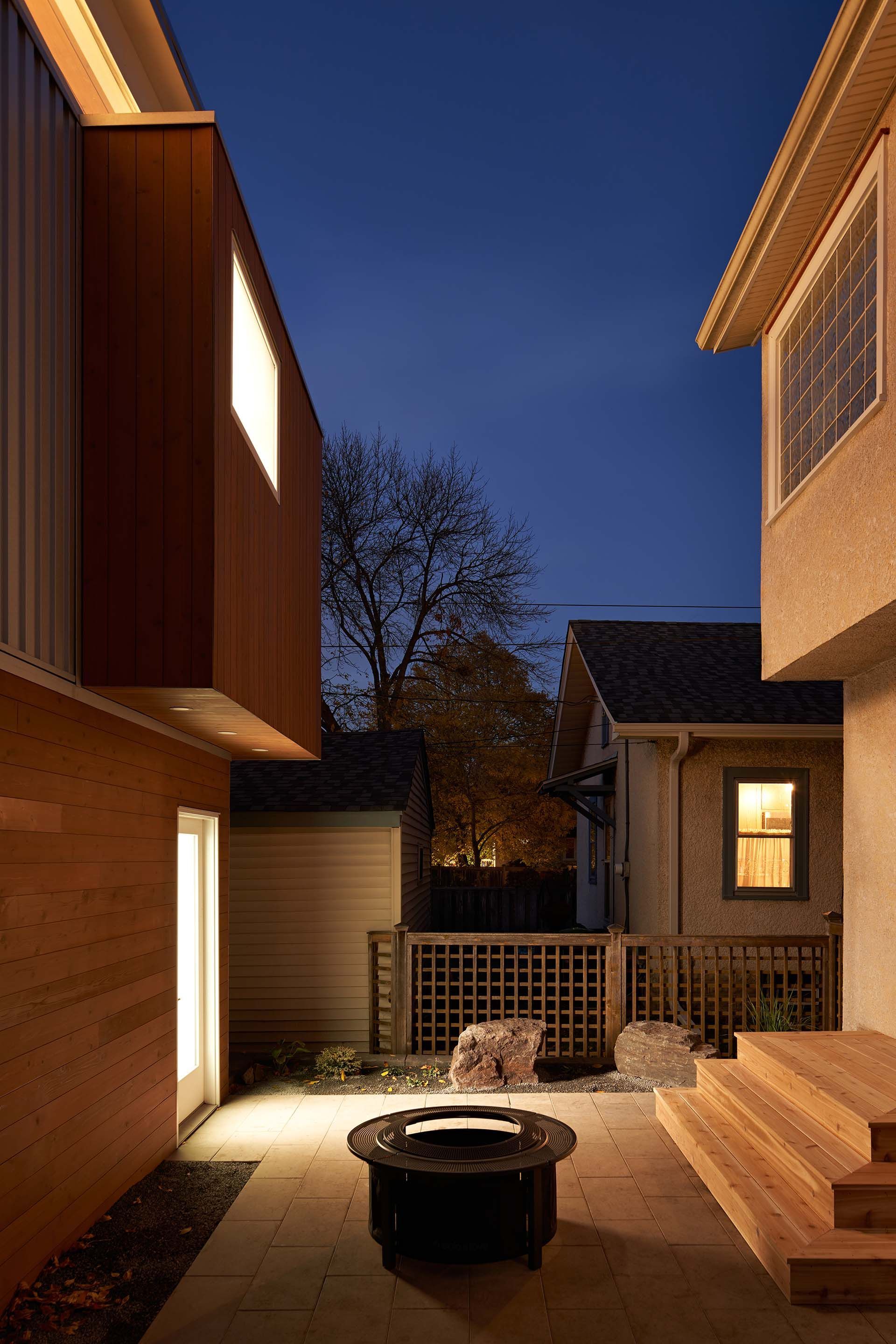 A patio with a fire pit between two houses at night