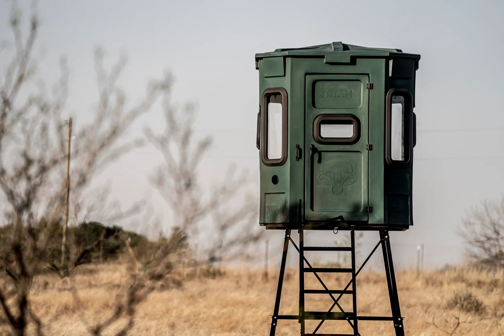 A green hunting blind is sitting in the middle of a dry grass field.