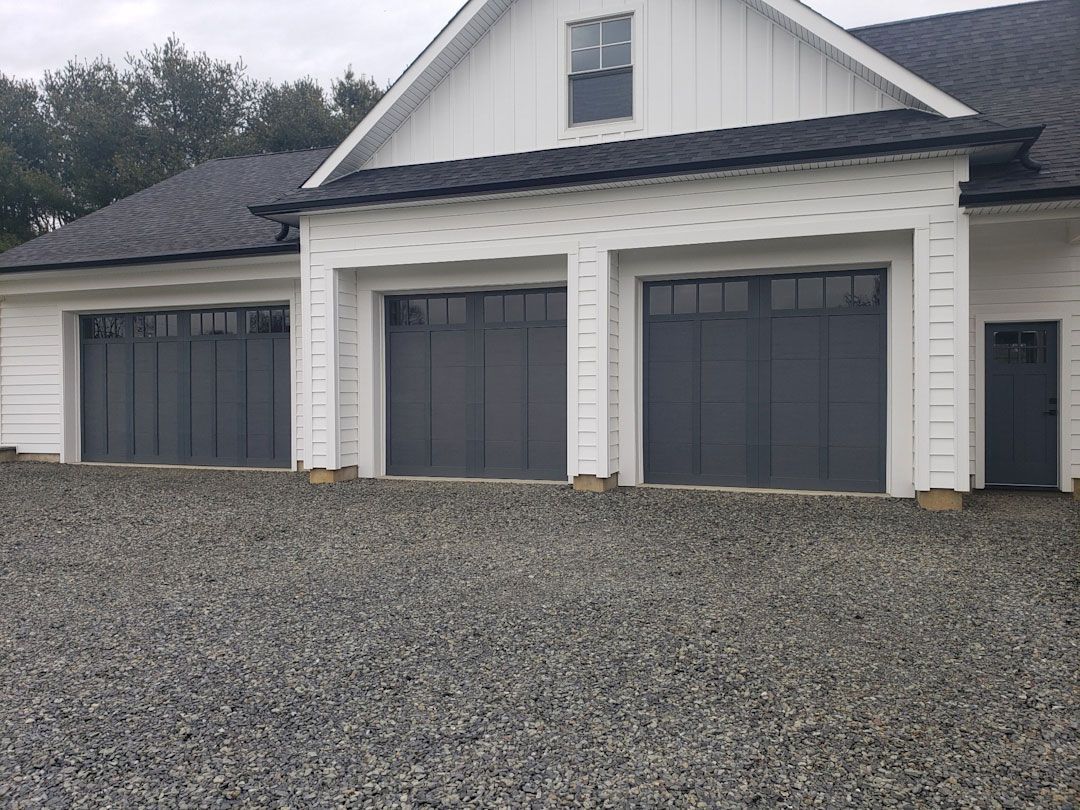 A white house with black garage doors and a gravel driveway in front of it.