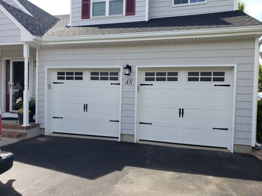 A white house with two white garage doors and a car parked in front of it.