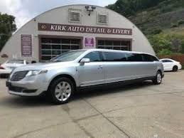 A silver limousine is parked in front of a building.