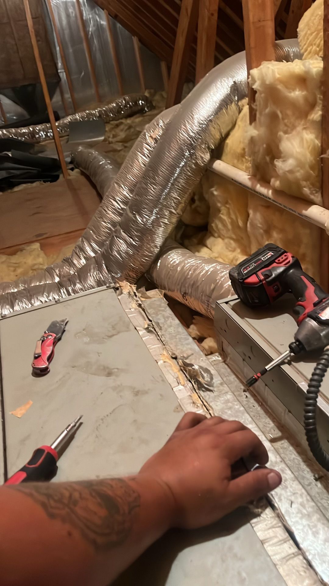 A man is working on an air duct in an attic.